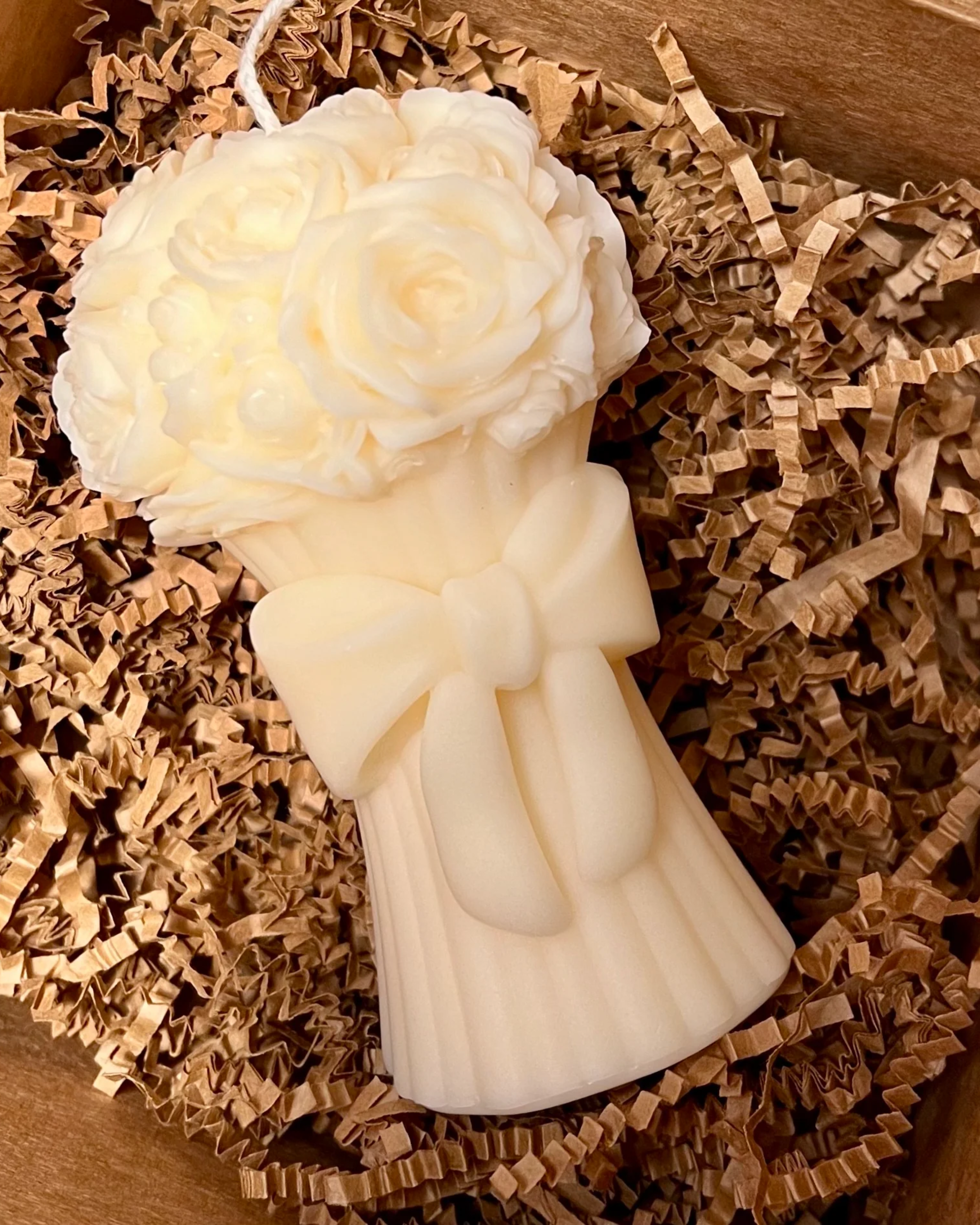 White angel-shaped candle with a bow on a bed of brown crinkled paper
