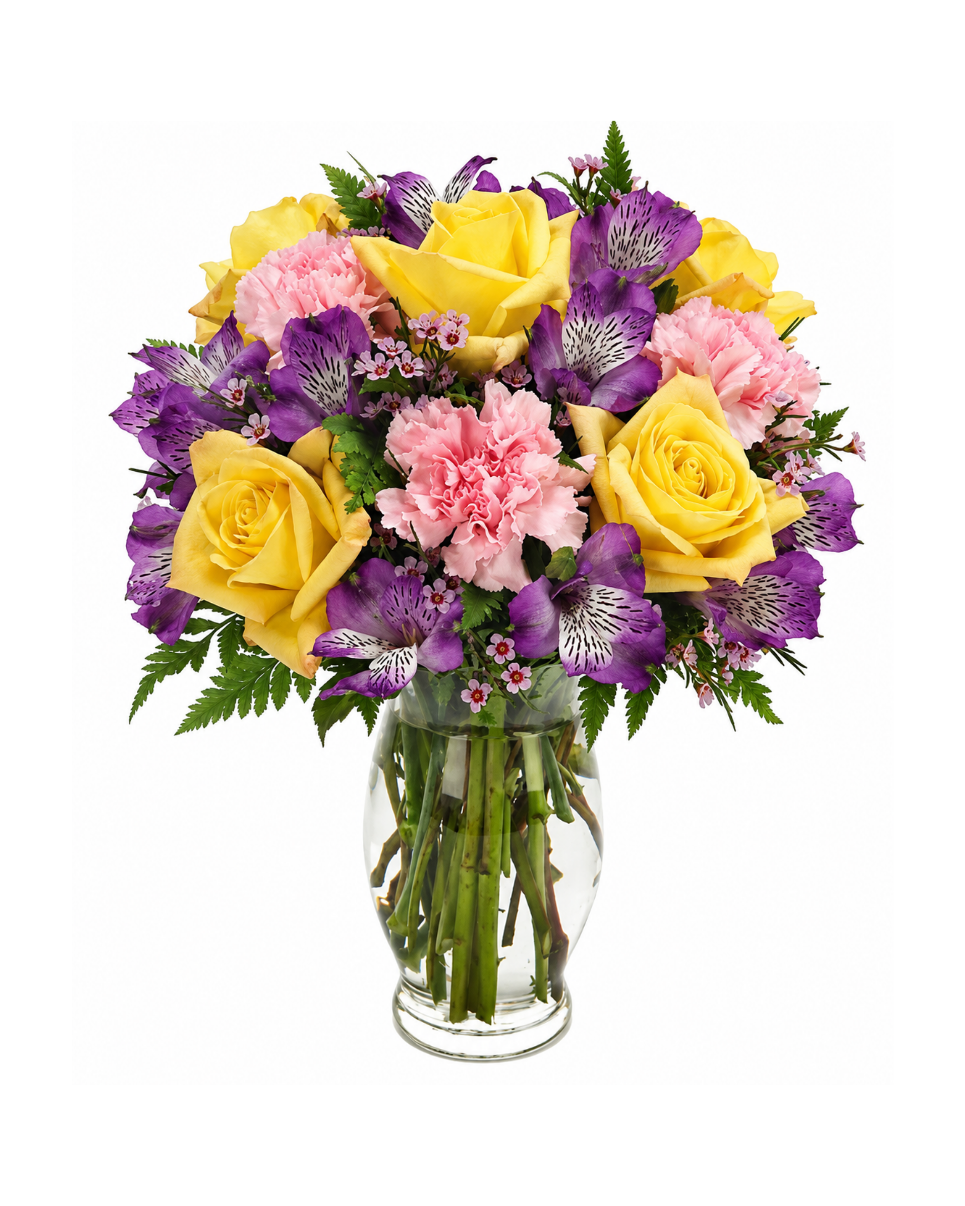 Bouquet of yellow roses, pink carnations, and purple flowers in a clear glass vase on a white background